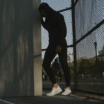 Athletic Shoes - a man in a black hoodie leaning against a fence